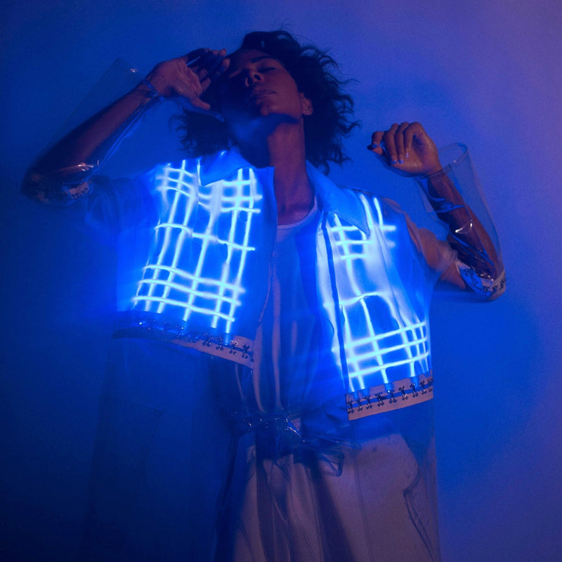 Woman in a clear Neon Cowboys LED 2-in-1 Plaid Trench Coat with the blue glowing plaid grid lit across the chest, a light up jacket and led costume statement piece for music festivals, raves, EDC and cyberpunk cosplay looks, Neon Cowboys