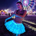 Smiling woman dancing in a cyan glowing Neon Cowboys LED 3 Layer Tiered Skirt by a festival Ferris wheel at night, a light up dress and led rave outfit stagewear favored by go-go dancers, festival dancers, showgirls and burlesque performers, perfect festival outfit for raves, EDC and Coachella, Neon Cowboys