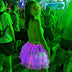 Woman glancing back in a pink and purple glowing Neon Cowboys LED 3 Layer Tiered Skirt amid a green-lit festival crowd, a light up dress and led rave outfit stagewear for go-go dancers, festival dancers and cabaret performers, an eye-catching festival outfit for raves, Coachella and EDC, Neon Cowboys