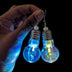 Hand holding pair of LED bulb earrings showing different colors - Close-up of color-changing light bulb-shaped jewelry demonstrating RGB lighting effects for rave outfits, costume parties, and statement accessories