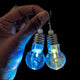 Hand holding pair of LED bulb earrings showing different colors - Close-up of color-changing light bulb-shaped jewelry demonstrating RGB lighting effects for rave outfits, costume parties, and statement accessories