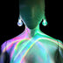 Woman wearing color-changing LED bulb earrings against dark background - Illuminated light bulb-shaped jewelry casting colorful reflections for music festivals, nightclub events, EDM concerts, and futuristic fashion looks