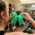 Cheerleader in the locker room tying a light-up LED cheer bow glowing green onto a teammate's high ponytail