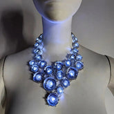 White mannequin bust wearing a chunky clear gem bib statement necklace glowing cool blue, a cool white LED light-up rhinestone jewelry piece with elegant CZ gems, an illuminated led necklace and light up necklace for weddings, formal events, brides and nightclub fashion, Neon Cowboys