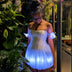 Woman in a Neon Cowboys LED Fairytale Dream Dress with a white glowing bubble skirt and puff sleeves among garden plants, a light up dress and led rave outfit stagewear for showgirls, burlesque performers and drag queens, a dreamy festival outfit for raves, Pride and bachelorette parties, Neon Cowboys