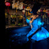 Woman sipping a cocktail in a Neon Cowboys LED Fairytale Dream Dress glowing cyan blue at a moody bar, a light up dress and led rave outfit stagewear for showgirls, burlesque performers and drag queens, a dreamy festival outfit for raves, EDM concerts and weddings, Neon Cowboys