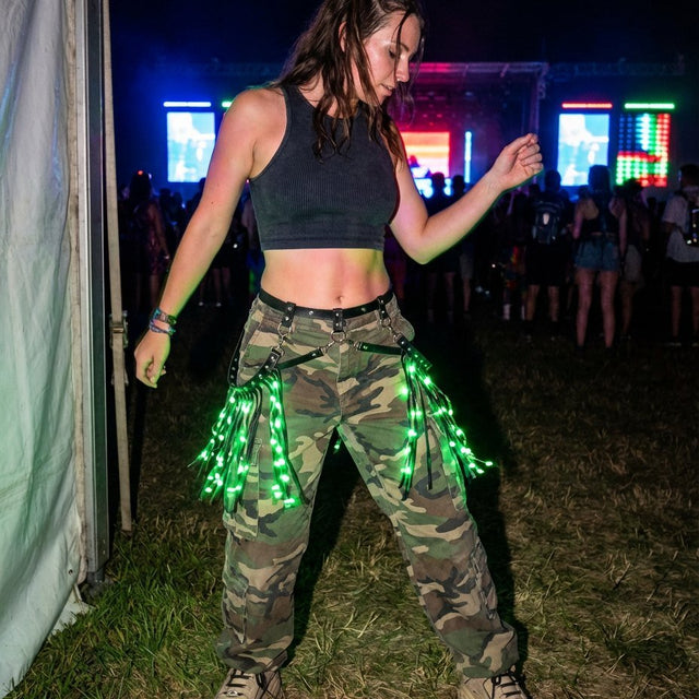 Woman in camo pants dancing at a night festival in a black LED fringe garter glowing green, a light-up garter with green glowing fringe and stagewear for festival dancers, go-go dancers and rave performers, perfect for music festivals, EDM concerts, raves and Pride, Neon Cowboys