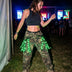 Woman in camo pants dancing at a night festival in a black LED fringe garter glowing green, a light-up garter with green glowing fringe and stagewear for festival dancers, go-go dancers and rave performers, perfect for music festivals, EDM concerts, raves and Pride, Neon Cowboys