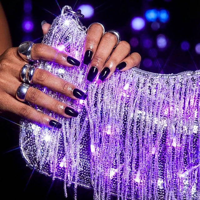 Close-up of hands holding a silver LED fringe purse glowing purple at a party, a glowing light up purse and light up fanny pack alternative perfect for raves, EDM concerts, festivals and Pride nights out, Neon Cowboys