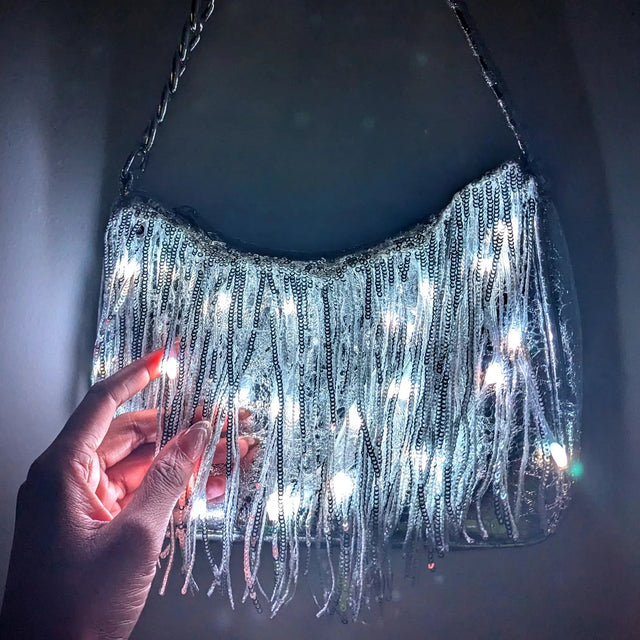 Close-up of a silver LED fringe purse glowing white against a dark backdrop, a glowing light up purse and light up fanny pack alternative perfect for raves, concerts, music festivals and disco cowgirl nights, Neon Cowboys