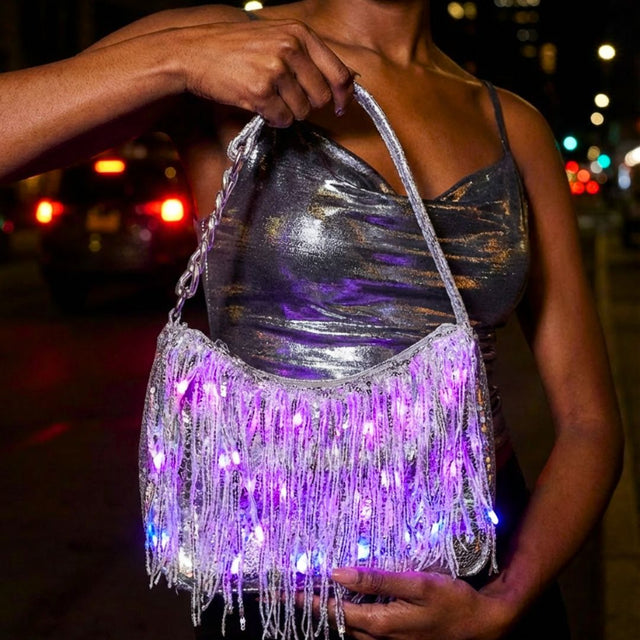 Woman on a city street at night holding a silver LED fringe purse glowing purple, a glowing light up purse and star-purse style bag perfect for raves, concerts, music festivals and disco cowgirl nights out, Neon Cowboys