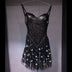 LED Fringe Sequin Dress by Neon Cowboys, a black light up sequin fringe dress with the fringe glowing white on a hanger, this led fringe sequin dress, led dress and light up dress with a led bodysuit base is space cowgirl and showgirl, go-go dancer and drag stagewear for raves, EDM concerts, festivals and bachelorette parties, Neon Cowboys