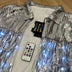 Silver LED sequin fringe jacket laid flat with accessories - Complete package contents showing jacket, remote control, and batteries for color-changing illuminated apparel