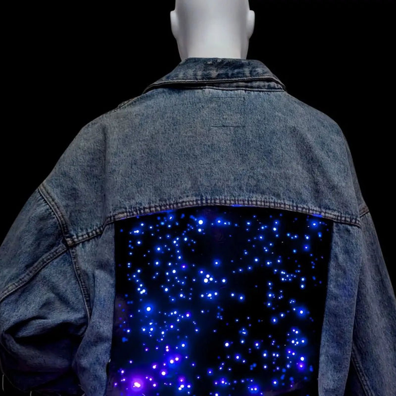 Back of a Neon Cowboys LED Galaxy Denim Jacket on a mannequin with blue starfield lights glowing across the light up back panel, a blue rainbow color changing led jacket and statement piece for music festivals and concerts, a space cowboy cowgirl outdoor rustic jean jacket, Neon Cowboys