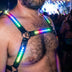 LED Harness by Neon Cowboys, a close up of a rainbow glowing light up chest harness with an O-ring worn at a night festival, this neon Pride harness and led harness for men is standout go-go dancer, drag and rave performer stagewear for festivals, EDM concerts, Pride and club nights, Neon Cowboys