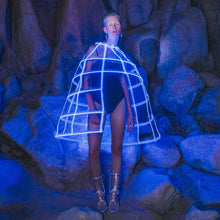 Woman wearing light up glowing blue LED hoop cage skirt structure against rock background perfect for avant garde fashion shows and futuristic festival outfits