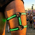 Close-up of a thigh wearing a green-glowing LED leg harness with silver O-ring straps at a festival, a color-changing light up harness and led harness thigh piece, performance stagewear for go-go dancers, drag and rave performers at EDM concerts, Neon Cowboys