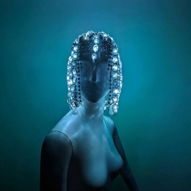 LED Rhinestone Gem Head Piece glowing under blue stage light — a color-changing light-up crystal headpiece with draping rhinestone strands that frame the face, a statement showgirl crown for burlesque, drag, cirque and festival performers.