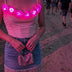 A woman at a festival wears the blush corset with LED light up roses glowing pink over a denim skirt, a light up corset and LED rose corset stagewear for go-go dancers, burlesque performers and festival dancers at raves, music festivals, and EDM concerts, Neon Cowboys LED rose corset, Neon Cowboys