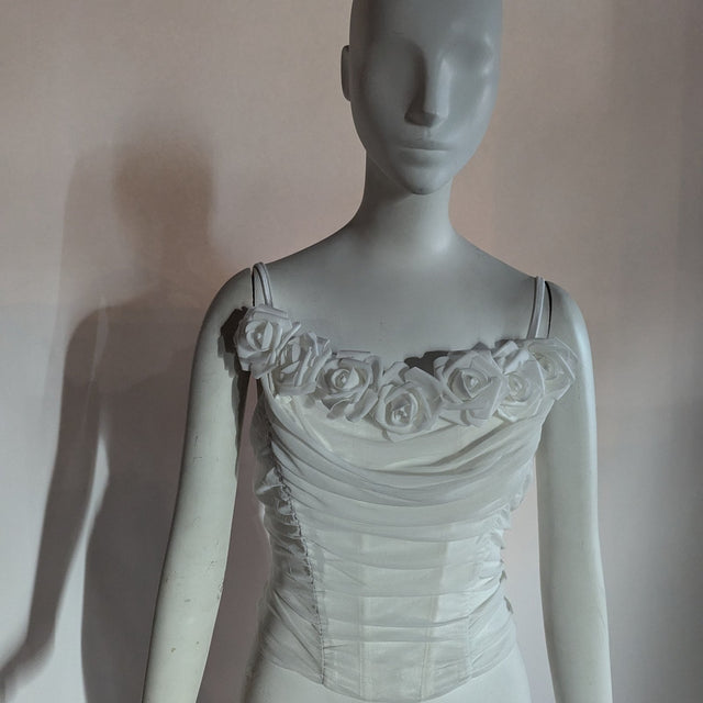 A white ruched rose corset on a mannequin with foam roses along the neckline shown with lights off, a light up corset and LED rose corset stagewear for go-go dancers, burlesque performers, brides and festival dancers at raves, weddings, and music festivals, Neon Cowboys LED rose corset, Neon Cowboys