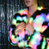 Close-up of a woman clutching a pastel rainbow color-changing LED faux fur crop jacket by a glitter curtain, a glowing light up rave coat and led costume for go-go dancers and showgirl performance outfits at Coachella, Pride and EDM concerts, Neon Cowboys