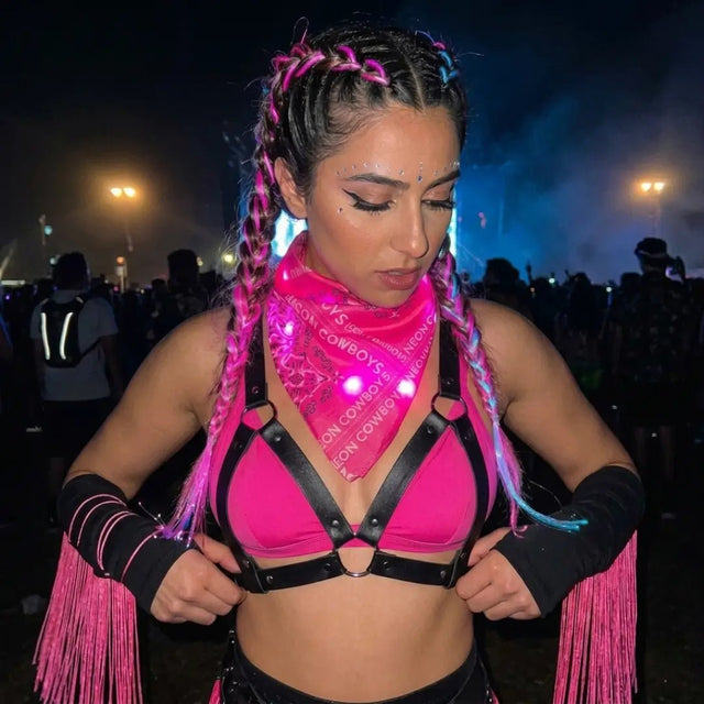 Woman at a night festival in a pink glowing LED light-up bandana and pink harness top, neon bandana and led bandana glow accessory for a rave, music festival or country concert, space cowgirl look, Neon Cowboys