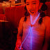 Woman wearing pink light up bolo tie at nightclub with red ambient lighting creating glowing cowboy fashion statement perfect for country music events and western cowgirl themed parties