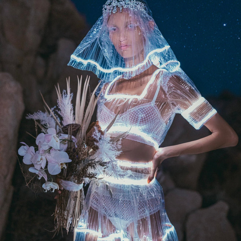 Bride in a glowing Neon Cowboys couture illuminated light up bridal veil and sheer LED wedding dress set holding a white bouquet at night, made-to-order light up wedding veil for LED weddings, magical evening reception photographs and unforgettable wedding entrances, Neon Cowboys