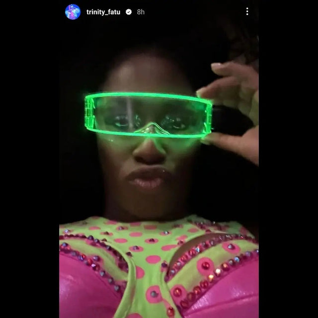 Performer in a pink rhinestone outfit wearing green glowing LED cyber glasses at night, futuristic light up glasses and space glasses for raves, music festivals, EDM concerts, drag shows, and stage performances, Neon Cowboys