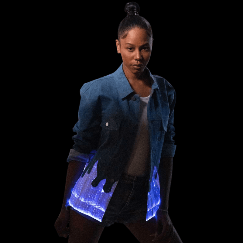 Woman in a light up flame denim jacket glowing blue flames on a black background, an LED jacket and light up jacket with fiber-optic flame hem for festival and rave stagewear, perfect for music festivals, EDM concerts, raves, Halloween costumes and Pride, Neon Cowboys