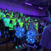 Cheerleaders holding glowing blue LED light-up pom poms at a blacked-out blacklight pep rally, far brighter than the neon glow-in-the-dark student section behind them — Neon Cowboys LED cheer & dance pom poms