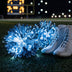 Pair of glowing blue LED light-up pom poms beside white cheer boots on a football field at night — battery-powered remote-controlled cheerleading pom poms in custom team colors for squads, dance teams and pom lines buying in bulk.