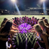 College cheer and dance squad huddled on a stadium field at night around glowing purple LED light-up pom poms — bulk custom team pom poms for cheerleading squads, dance teams, drill teams and pom lines in matching team colors.