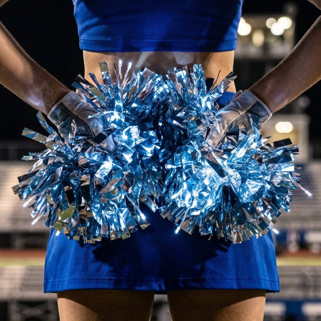 Close-up of a cheerleader holding a pair of glowing blue and silver metallic LED light-up pom poms — professional remote-controlled color-changing cheerleading pom poms available in custom team colors for bulk squad and dance team orders.