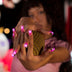 Woman holding a mesh ball at a night carnival with pink glowing LED light-up press-on nails, wireless led nails and light up nails that glow for a rave, music festival or EDM concert, Neon Cowboys