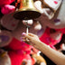 Hand ringing a carnival bell with soft pink glowing LED light-up press-on nails, wireless led nails and light up press on nails that glow for a rave, EDM concert or bachelorette, Neon Cowboys