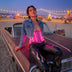 A person on a vintage car at Burning Man in a glowing pink light up LED PVC corset and denim jacket at dusk, a unisex glowing neon light up corset and led rave outfit, glowing stagewear for go-go dancers and burlesque performers at Burning Man, raves and music festivals, Neon Cowboys