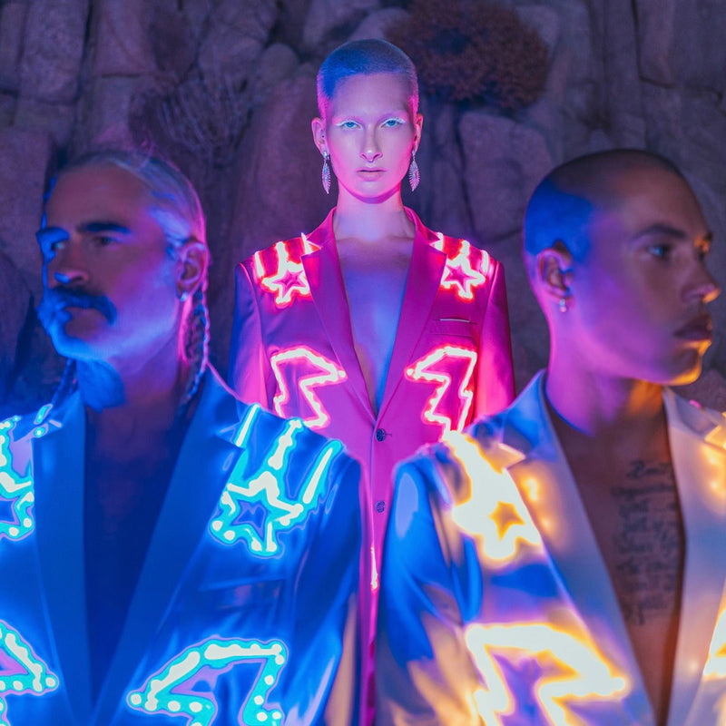 Three models in glowing pink and blue LED light-up nudie suits at night, illuminated LED costume stagewear perfect for nightclub performances, music festivals and fashion runway shows with cutting-edge light technology, made for go-go dancers, drag and cabaret showgirls, disco cowgirl concerts and Pride, Neon Cowboys