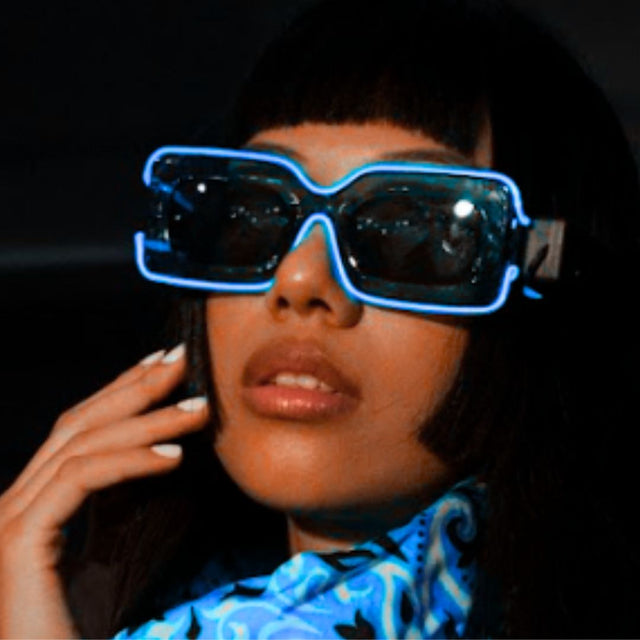 Woman sitting on concert bleachers at sunset in blue glowing LED light up party sunglasses, futuristic festival sunglasses and cyberpunk led glasses for concerts, raves, and country concerts, Neon Cowboys