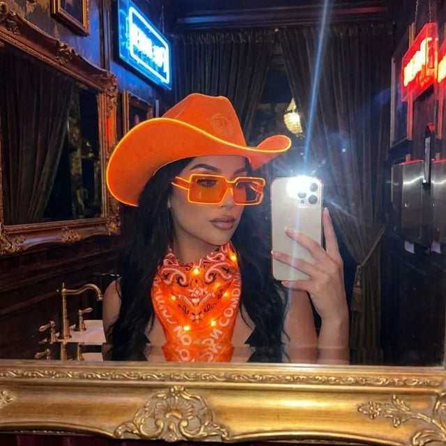 Woman in an orange light up cowboy hat and orange LED party sunglasses taking a mirror selfie, glowing festival sunglasses and cyberpunk led glasses for raves, country concerts, and EDM events, Neon Cowboys