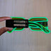 Battery pack detail of green glowing LED light up party sunglasses held against a plain wall, showing the rechargeable glow feature of these futuristic festival sunglasses for raves, EDM concerts, and glow parties, Neon Cowboys