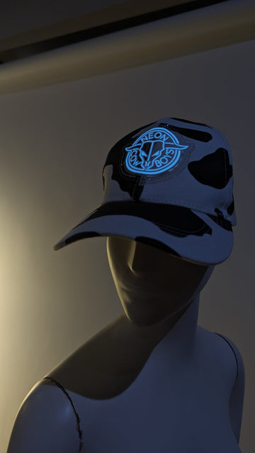 Black and white cowprint baseball cap with a glowing blue Neon Cowboys logo on a mannequin head