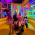 Four friends in glowing pink LED light-up mini cowboy hats on a yellow couch at a neon lounge, matching neon cowgirl hats and space cowgirl accessories for bachelorette parties, raves, music festivals and girls nights, Neon Cowboys
