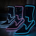 Three black light up boots glowing white, pink and blue lined up in a studio, these Out Past Midnight light up cowboy boots and light up heels come in colors for raves, music festivals and bachelorette parties, Neon Cowboys