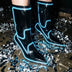 A model in black boots glowing blue standing on silver confetti at a night party, these Out Past Midnight light up cowgirl boots and light up heels are made for raves, New Year's Eve parties and nightclub nights, Neon Cowboys