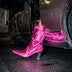 A model stepping out of a car at night in hot pink glowing LED light up boots, these Out Past Midnight light up cowgirl boots and light up heels are made for raves, Vegas nights and bachelorette parties, Neon Cowboys