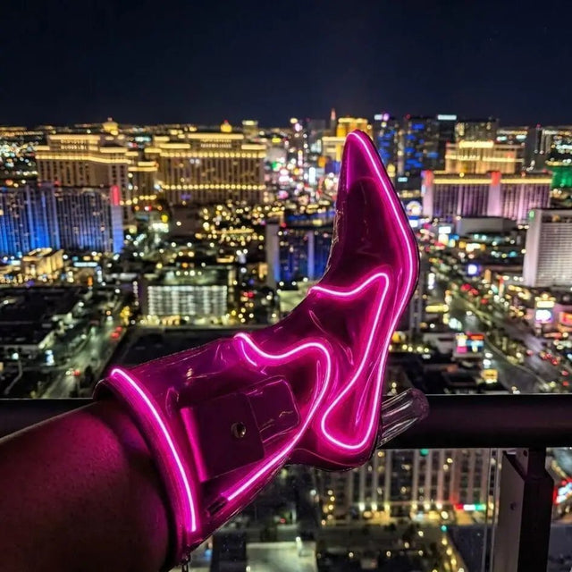 A raised leg showing a pink glowing LED light up boot against the Las Vegas skyline at night, these Out Past Midnight light up cowboy boots and light up heels are made for Vegas nights, raves and bachelorette parties, Neon Cowboys