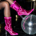 A model in pink glowing LED light up boots beside a disco ball on a dark floor, these Out Past Midnight light up cowboy boots and light up heels are made for raves, music festivals and bachelorette nights, Neon Cowboys