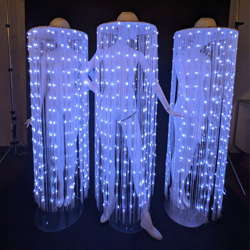 Neon Cowboys Remote Controlled LED Fringe Cowboy Hats glowing white-blue with full floor-length fiber-optic fringe cascading to the floor on three performers — color-changing light-up performance costume for touring dancers, drag shows, go-go and event entertainment