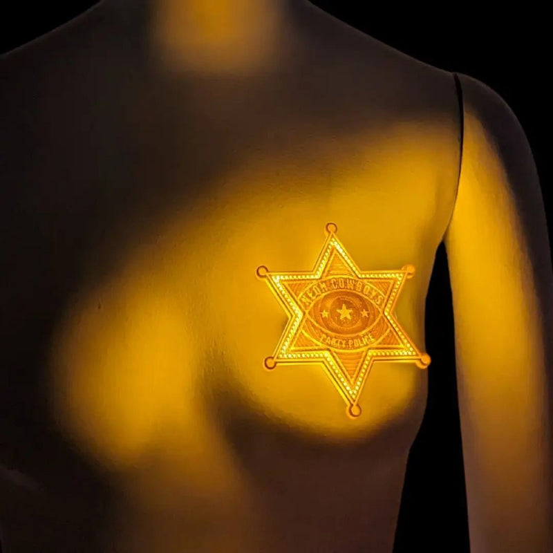 A glowing gold Party Police LED sheriff badge lit up on a mannequin chest in a dark setting, an illuminated 3D printed police accessory and light up costume piece for Woody costumes, space cowgirl outfits, western themed parties, music festivals and Halloween events, Neon Cowboys